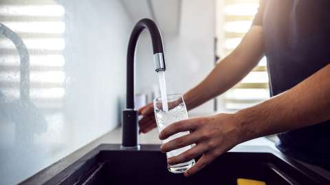 Hands holding a glass under a running faucet