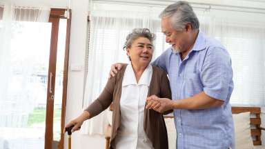 Older person with cane in home with another person guiding them