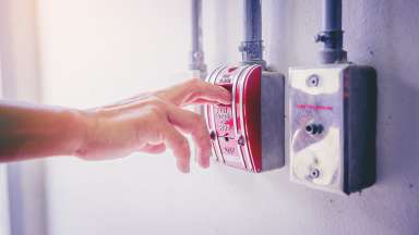 A hand is reaching to activate a fire alarm on a wall.