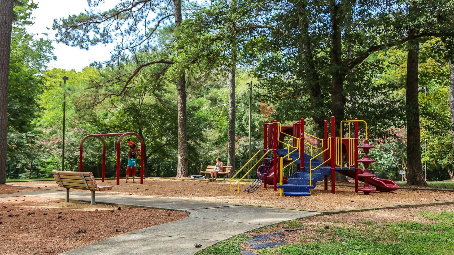 Parent pushing a kids on a swing and woman seated on a bench at the Biltmore Hills playground.