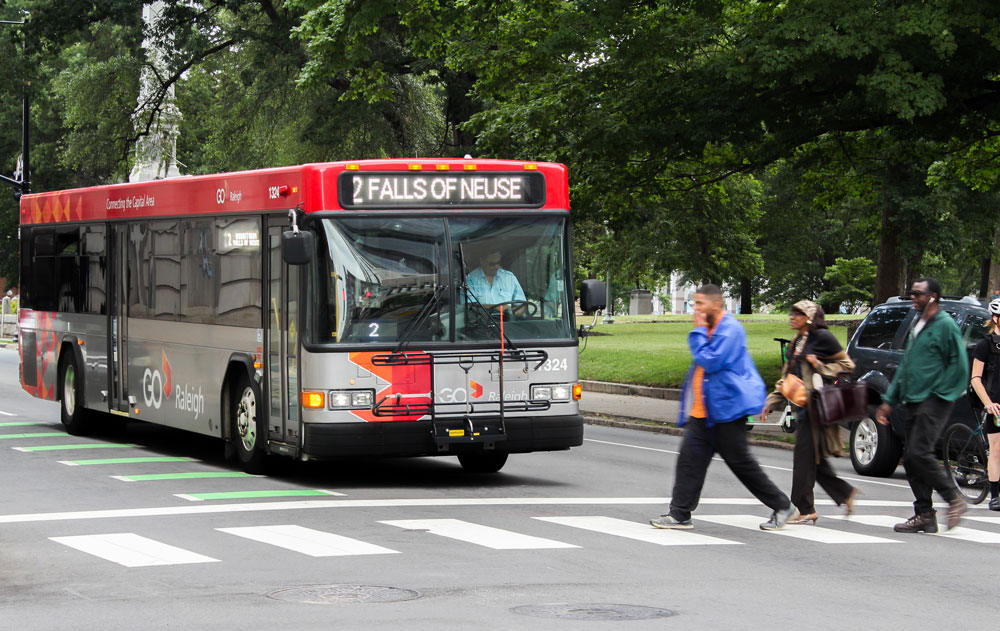 Group of walkers on a cross walk with a GoRaleigh bus in the background