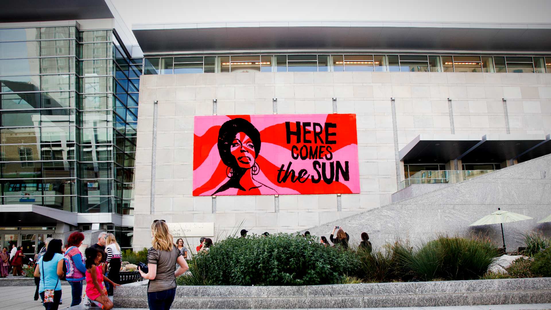 Large scale crocheted portrait of Nina Simone with the words "Here Comes the Sun" hanging on the outside of the Raleigh Convention Center.