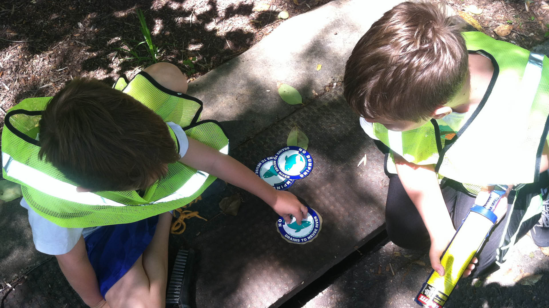 Kids in yellow vests marking storm drains with educational messages