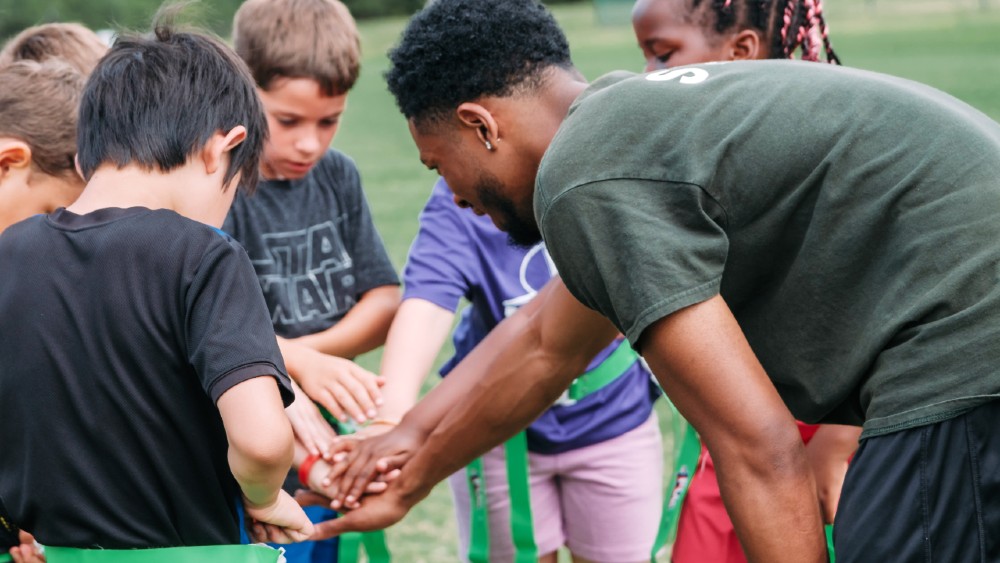 Kids in huddle with camp counselor with hands in