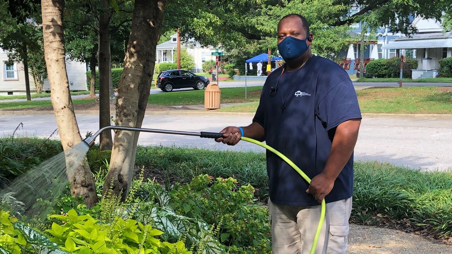 Man holding sprinkler over green bushes
