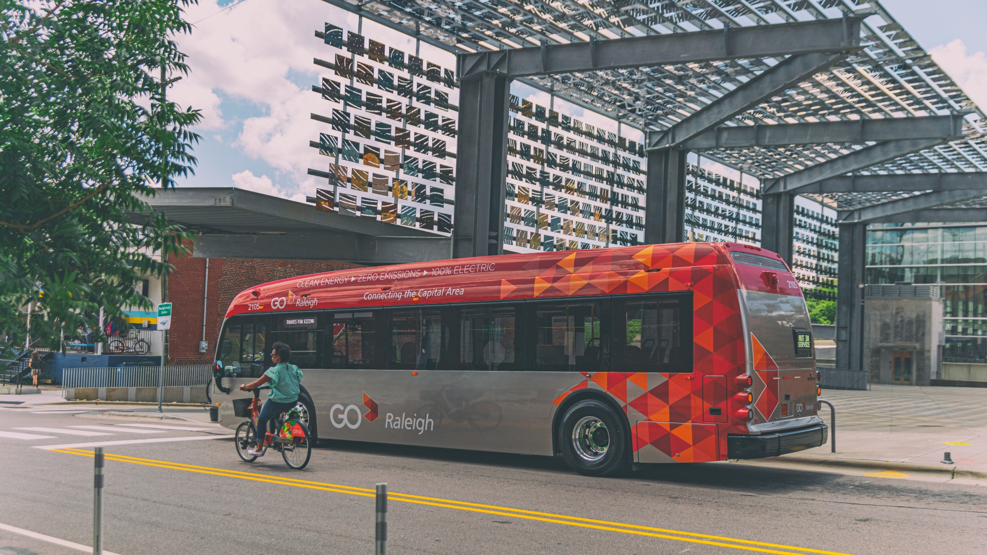 GoRaleigh Bus in front of metal awning of Raleigh Union Station. Woman on Citrix Cycle rides beside the bus