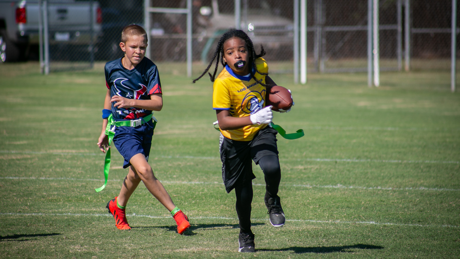 One boy running to make a touchdown being chased by an opponent.