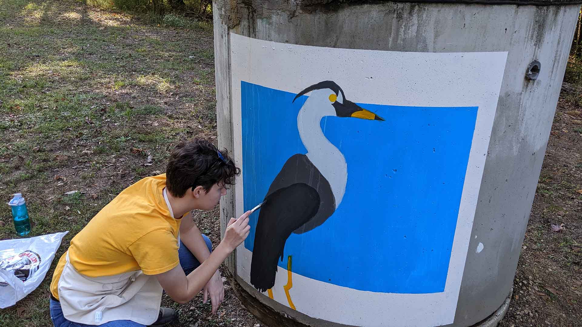 An artist paints a bird on a sewer up next to a Raleigh greenway