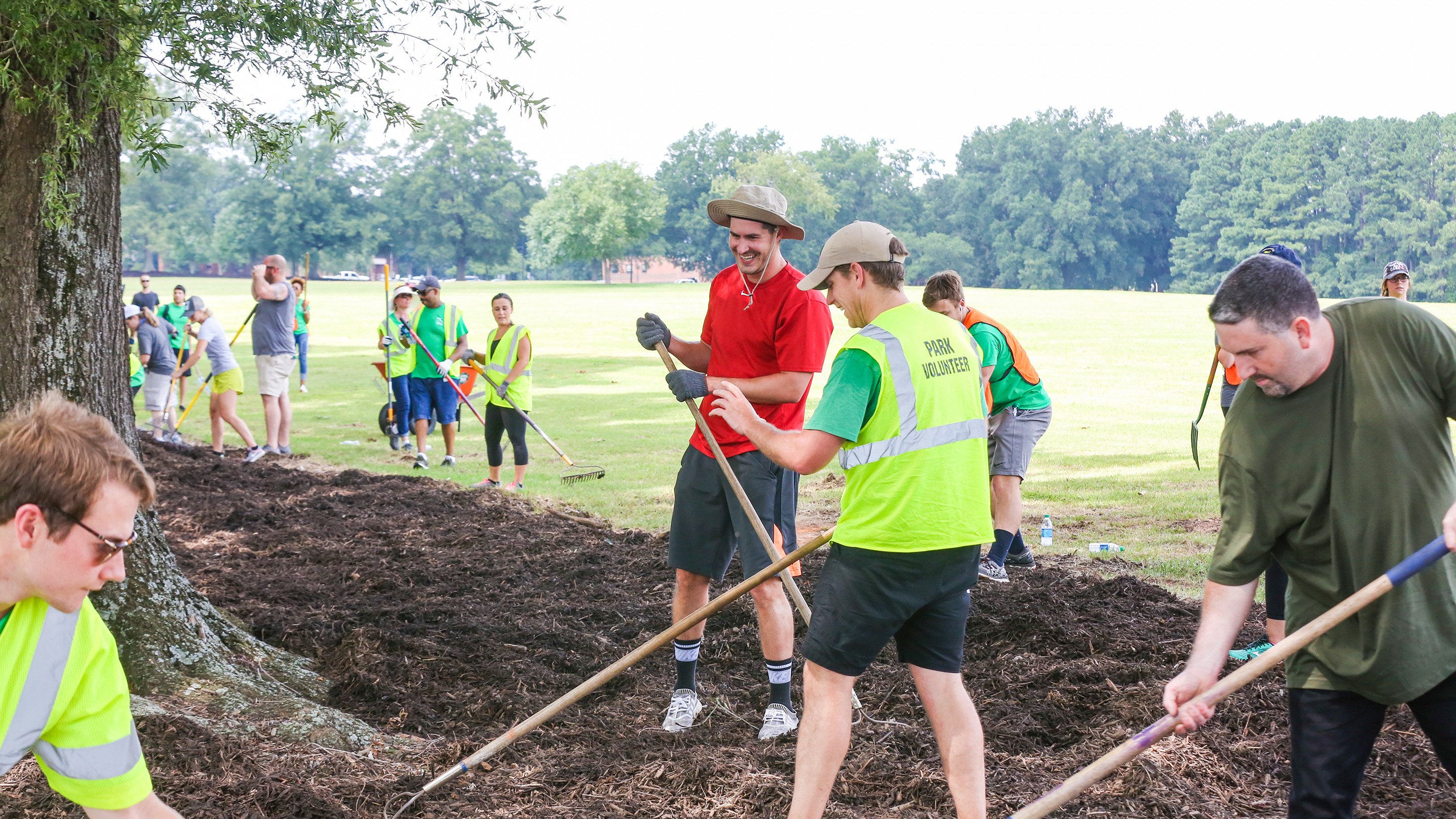 people smiling in safety vests with mulch and pitchforks