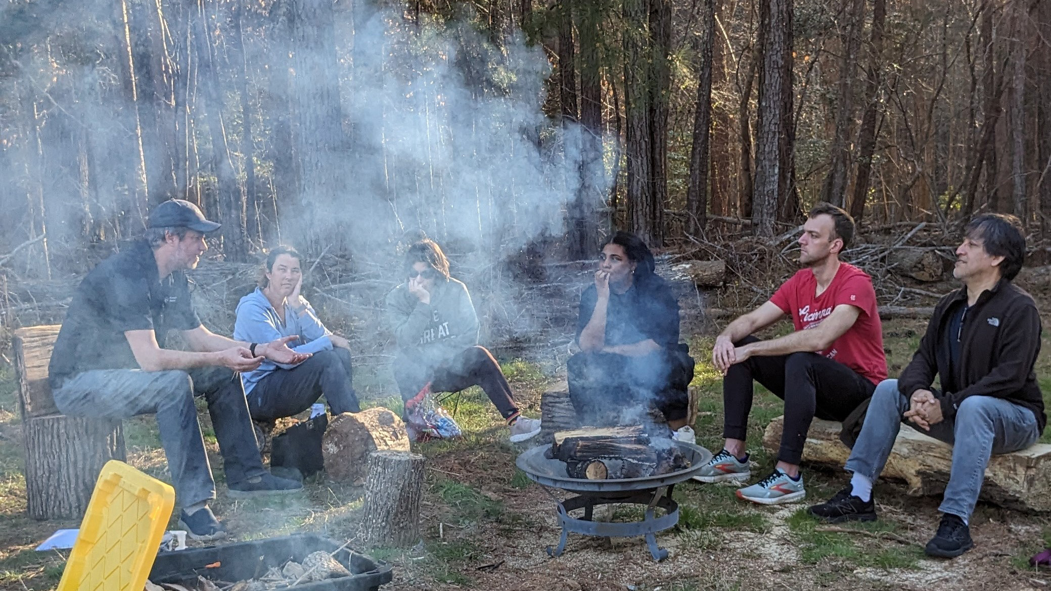 a group of people learning outdoors around a campfire