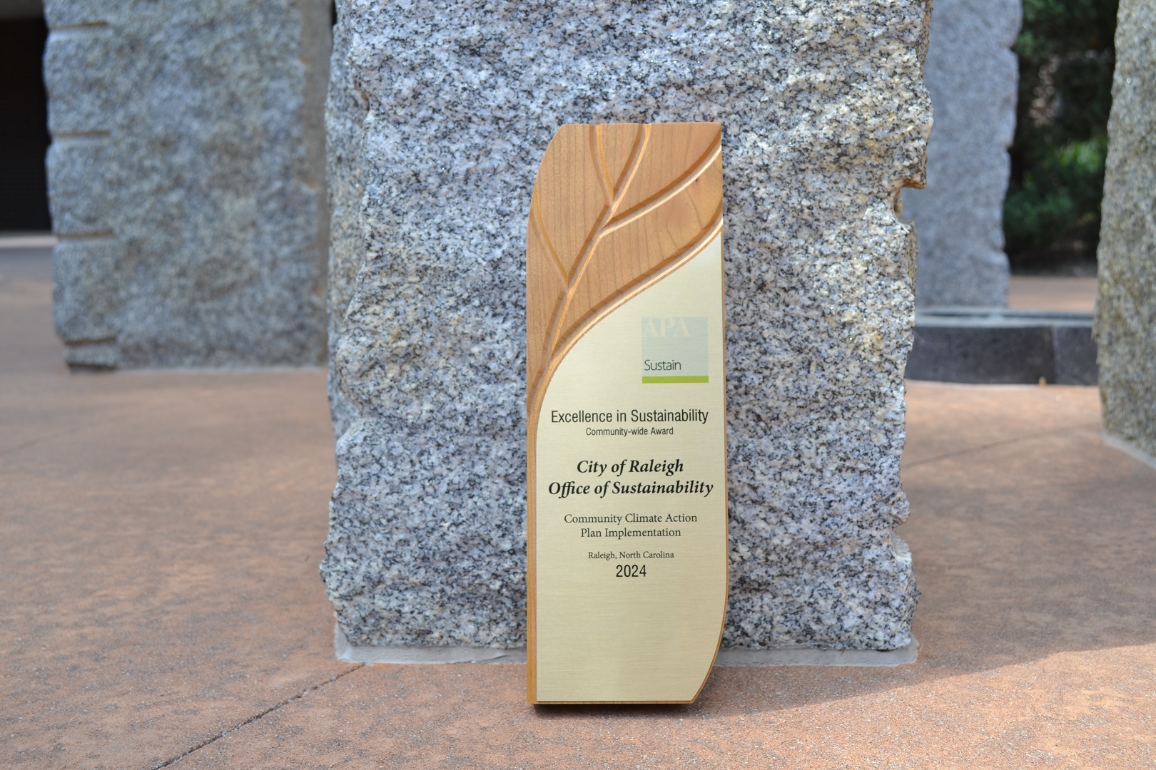 A wooden leaf shaped trophy displaying the City Of Raleigh Office of Sustainability's Award from the 2024 American Planning Association's Excellence in Sustainability Awards.  
