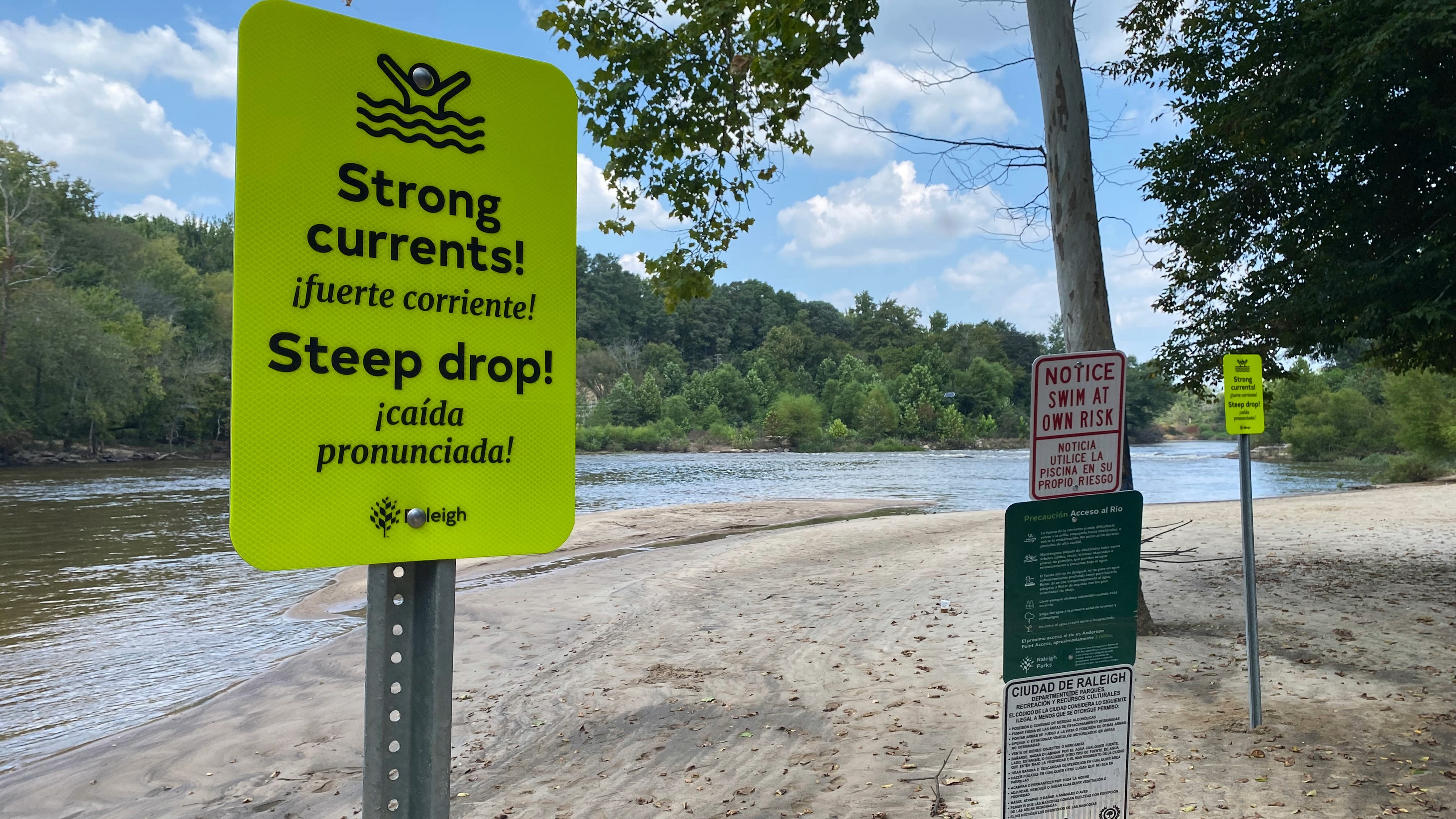 Image with the Neuse River in the background. The focus of an image is a safety sign that says "Strong Currents! Steep Drops!"