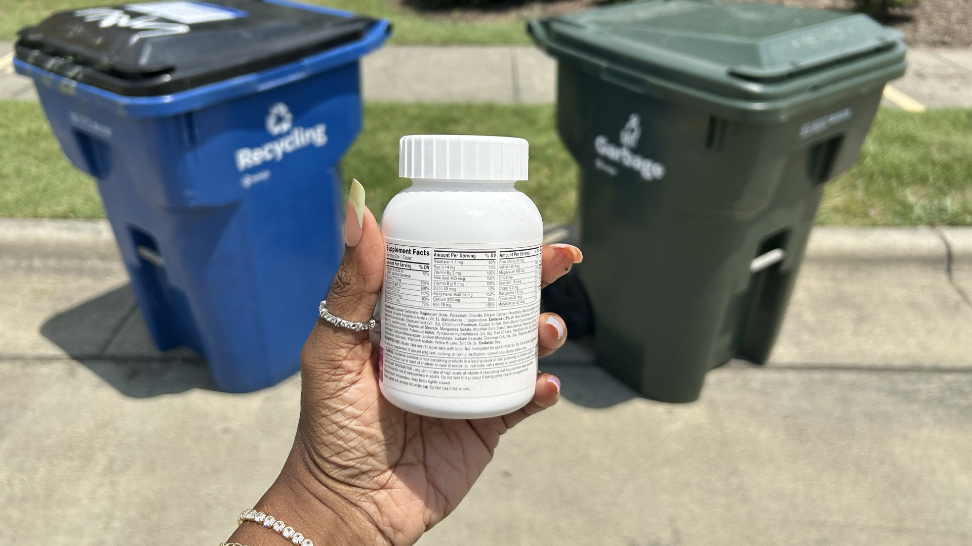 pill bottle held in front of a trash and recycling cart