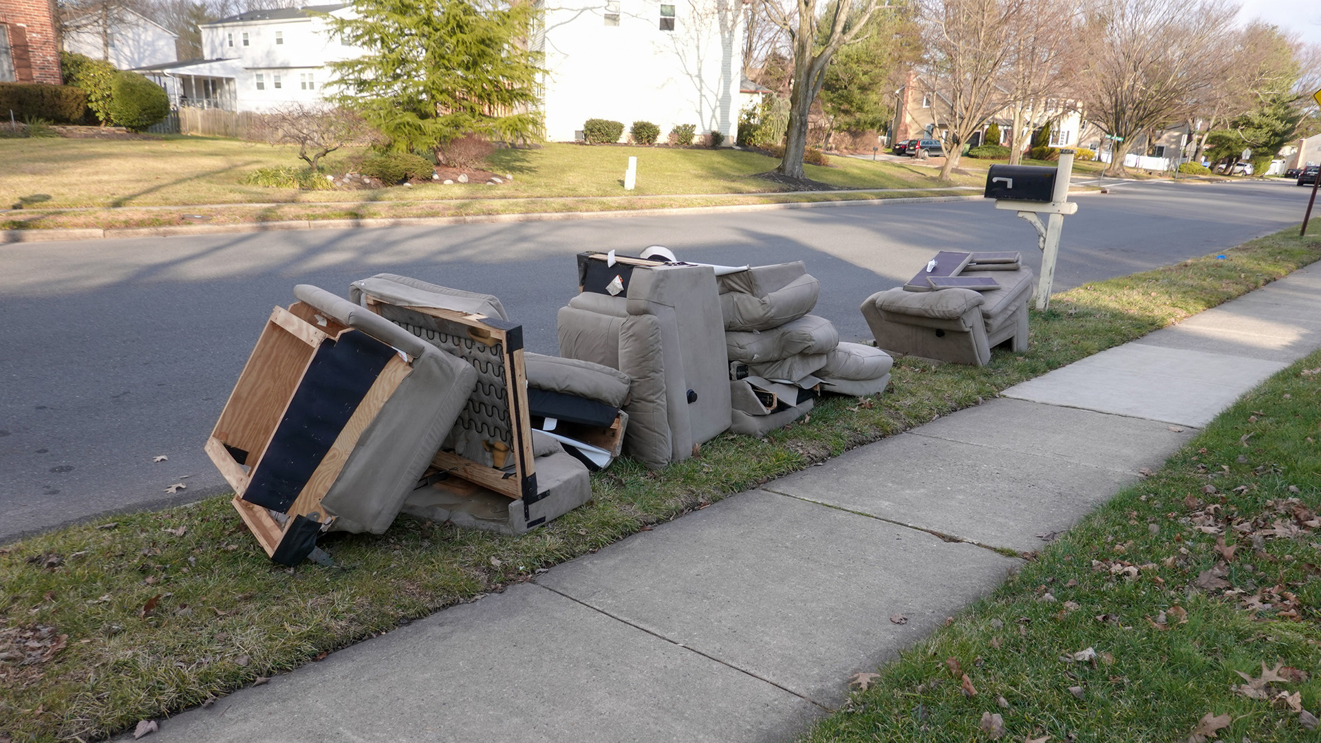 A discarded sofa sitting curbside on a neighborhood street with a sidewalk and mailbox in view. 