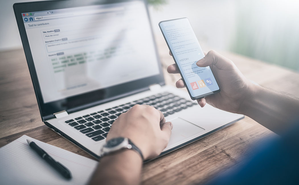 Person using a phone while working with a laptop.