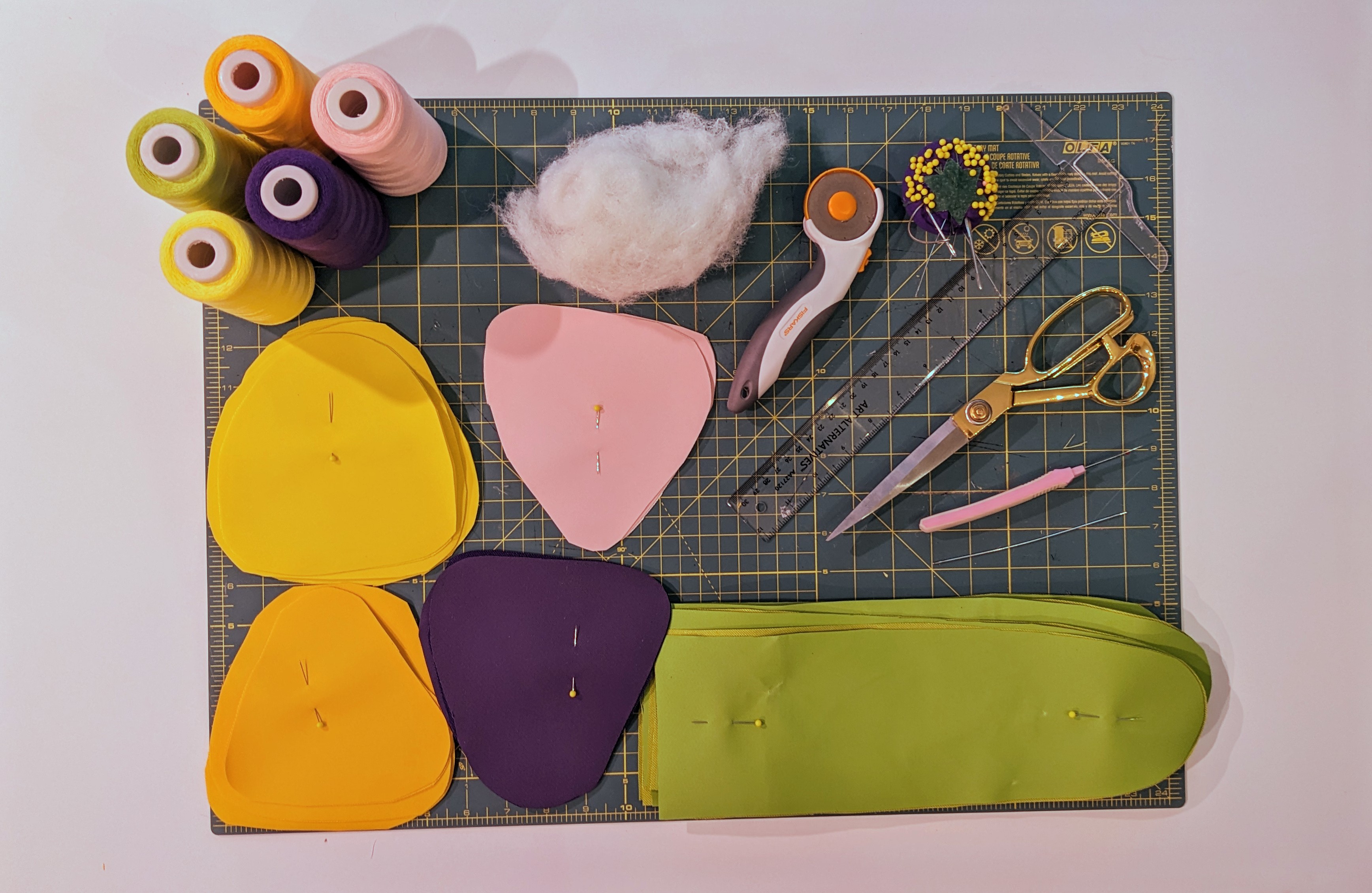 A cutting board covered with sewing tools, fabric and thread, the starting bits of a soft botanical sculpture,