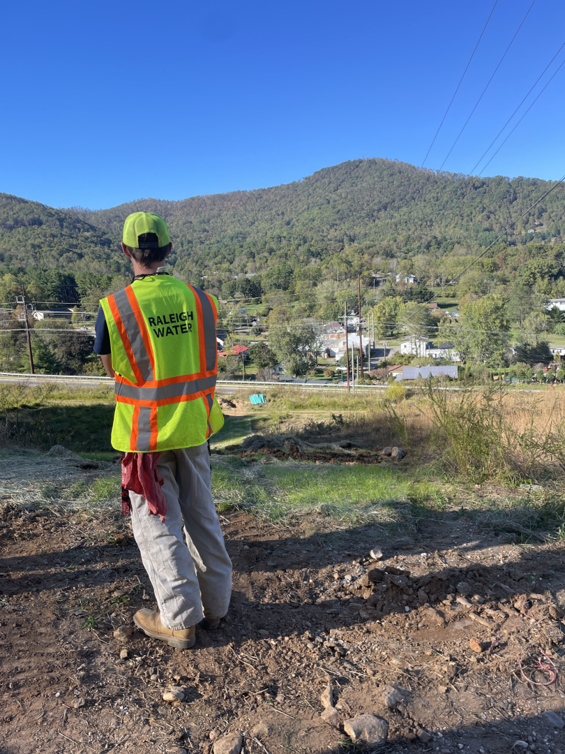 Raleigh Water employee standing in front of mountains in Western North Carolina, wearing a safety vest.