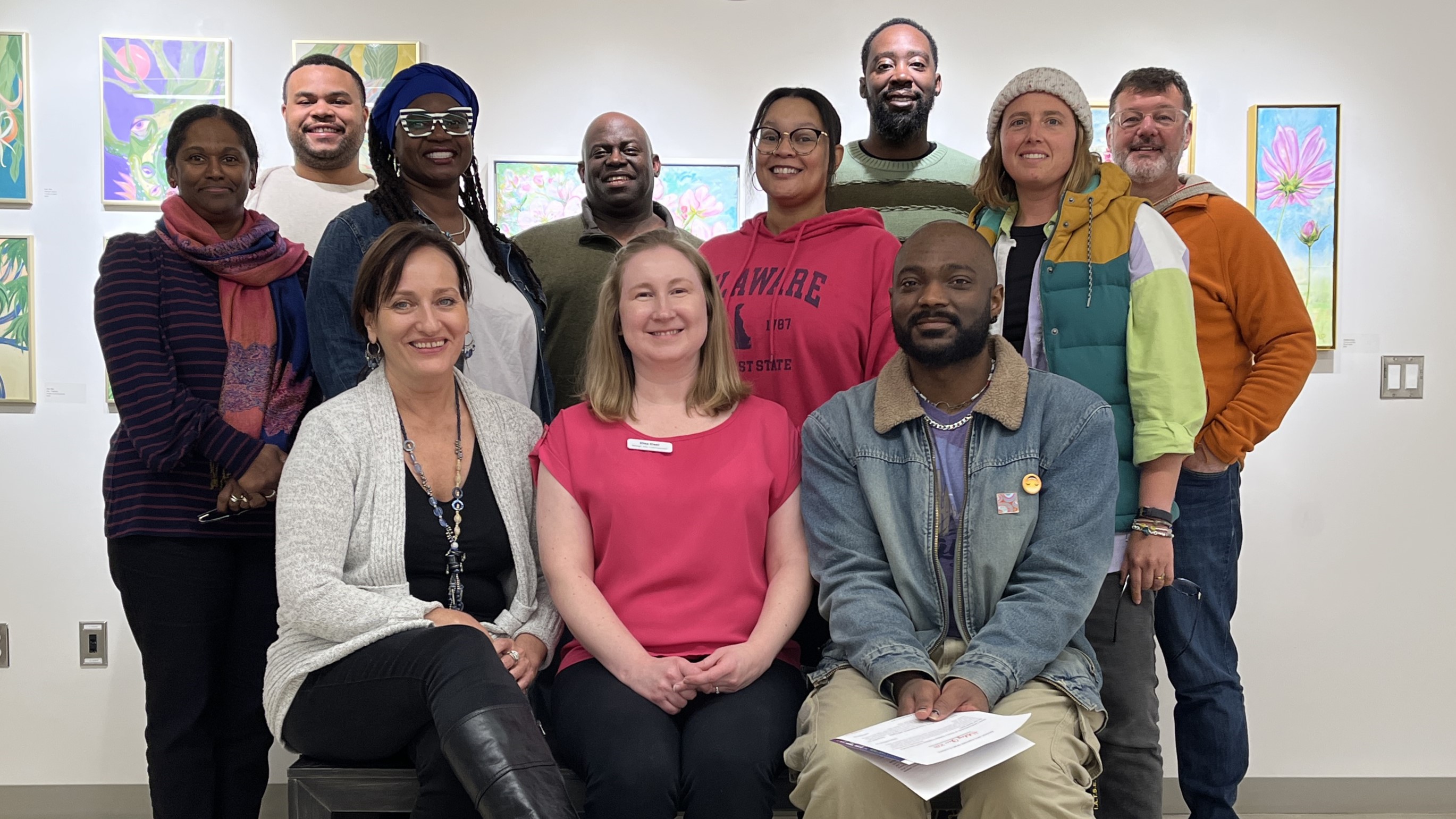 A group of 12 people smiling for the camera in an artsy setting.