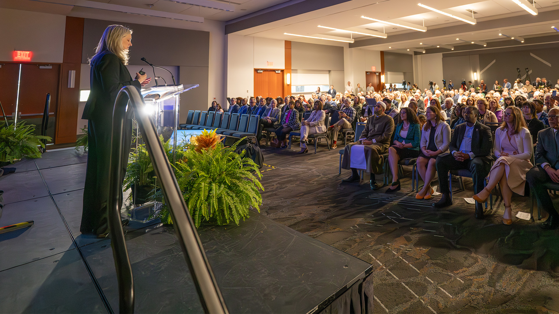 Mayor Cowell speaks at a podium on the stage with the audience looking on