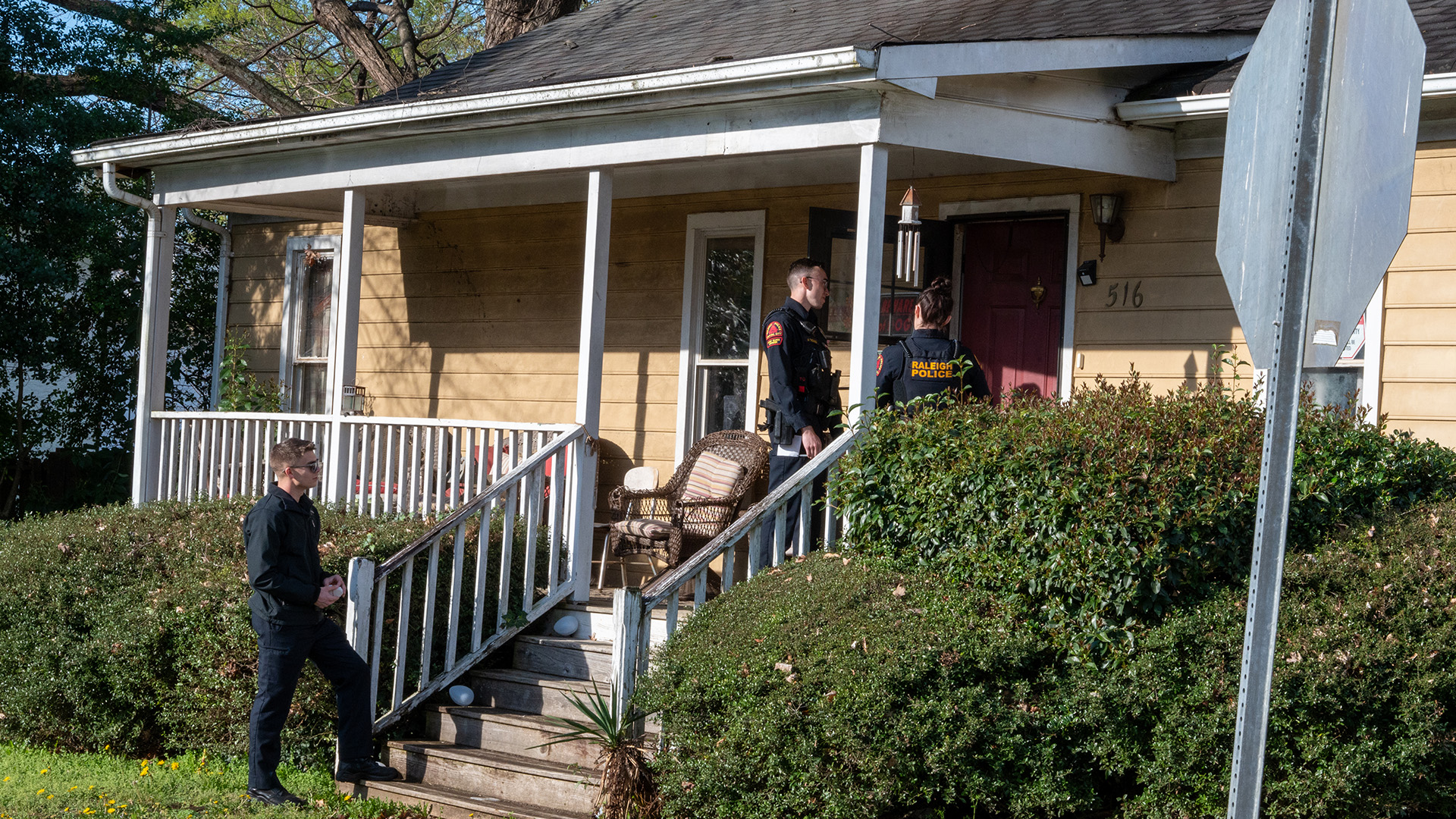 Three Raleigh officers stand on a porch talking with a resident.