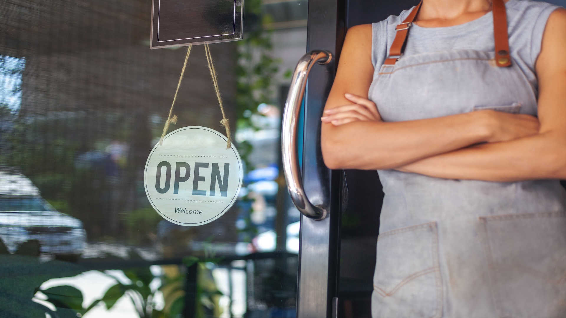 Photo of shop owner wearing apron standing next to "Open" sign