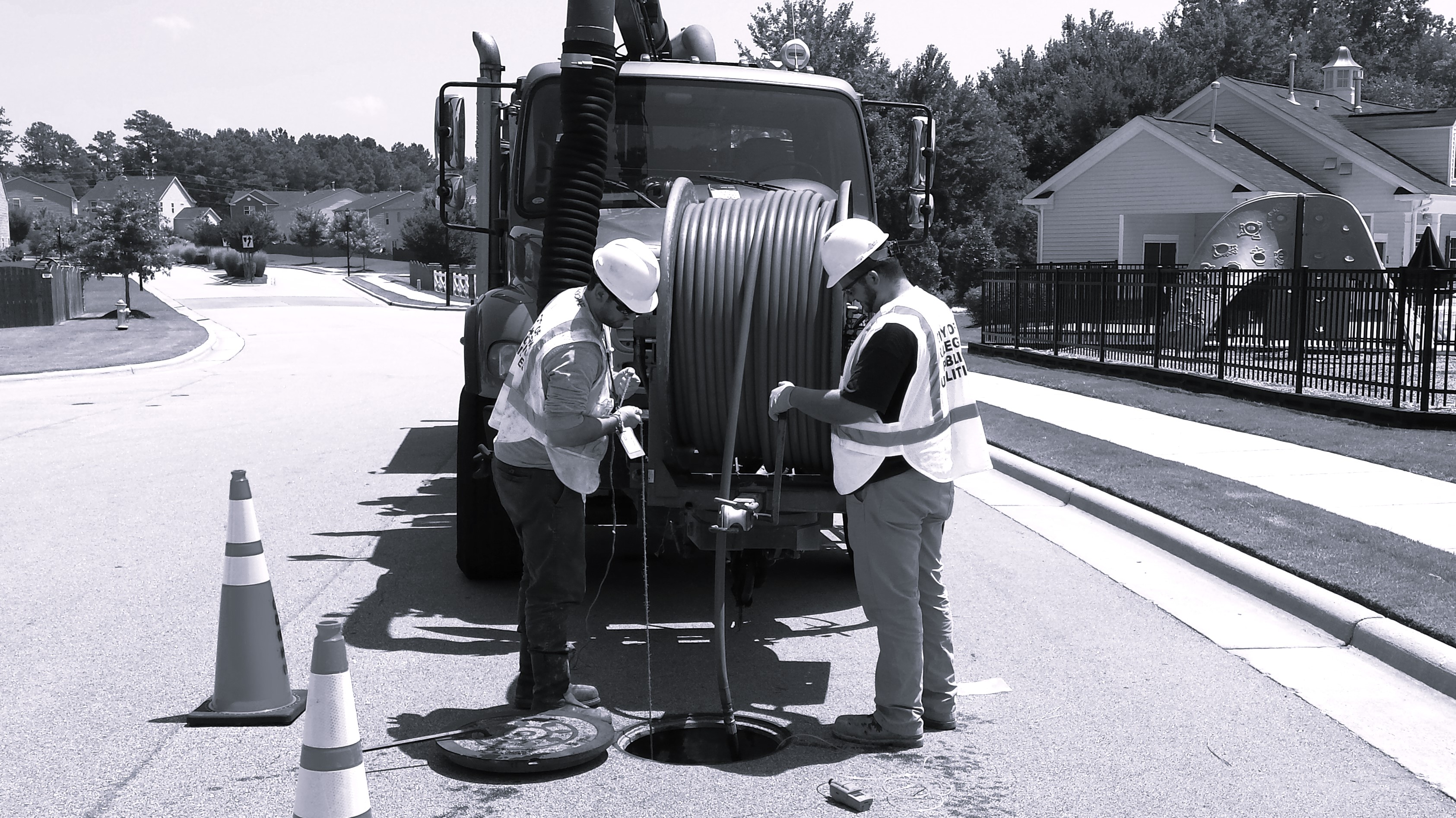 workers standing over open manhole in front of a work truck