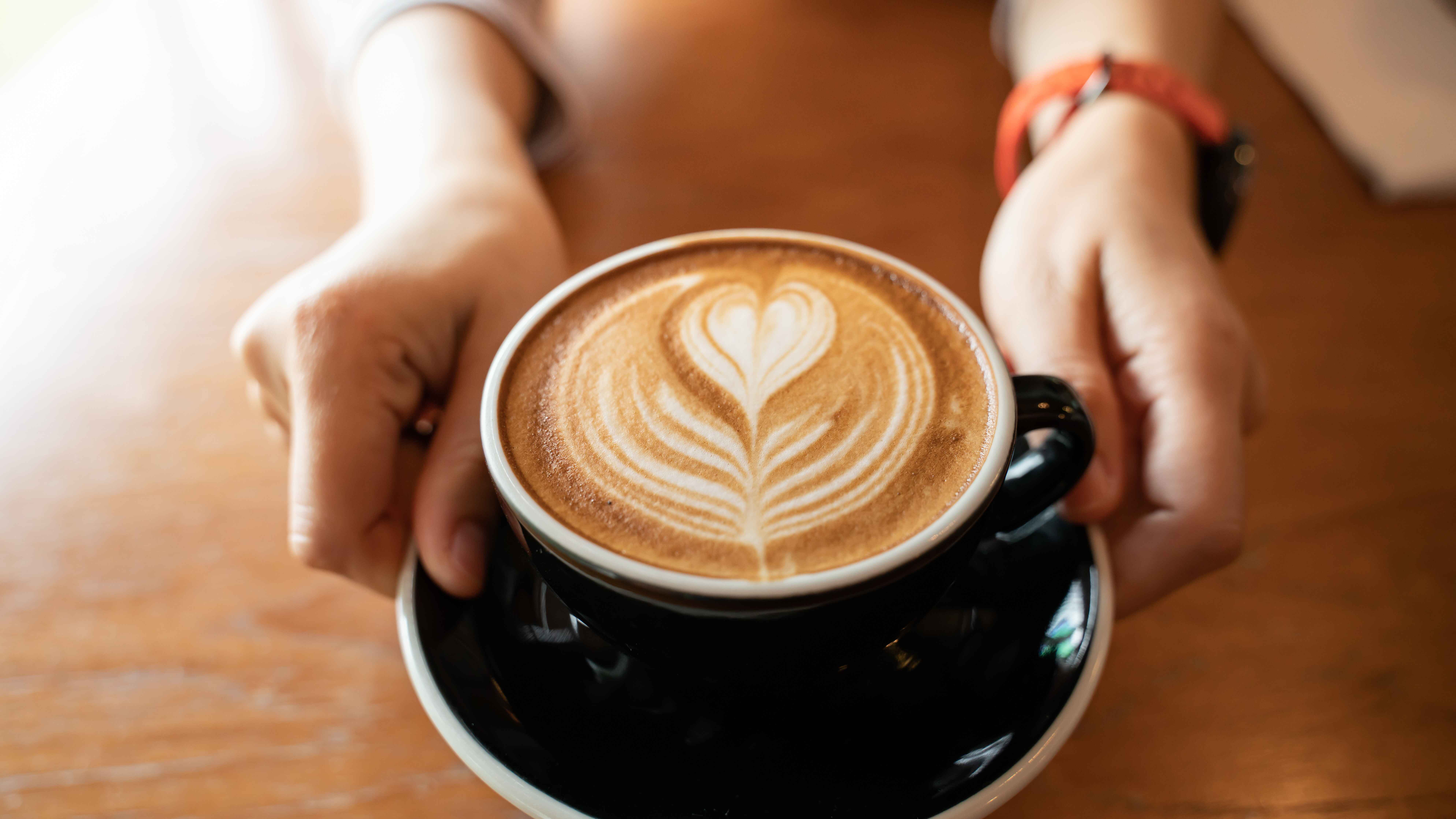 Pair of hands holding latte on a wooden table