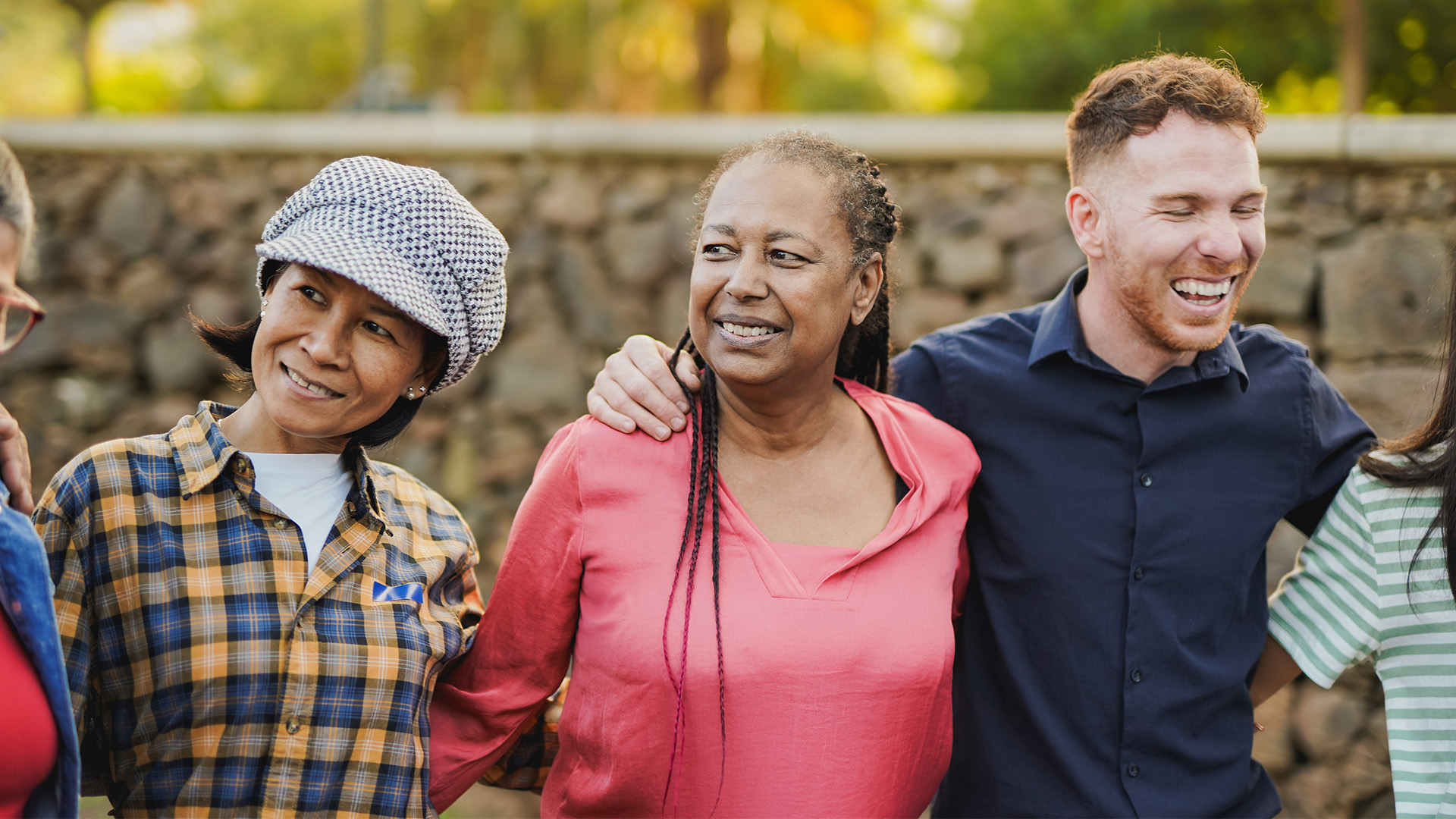 three diverse people smiling and laughing standing in a line with arms around each other