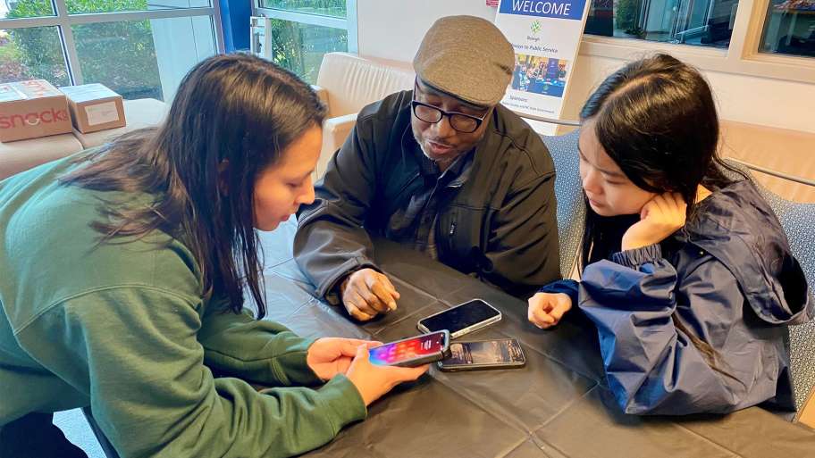 Two young women help a senior with his iphone