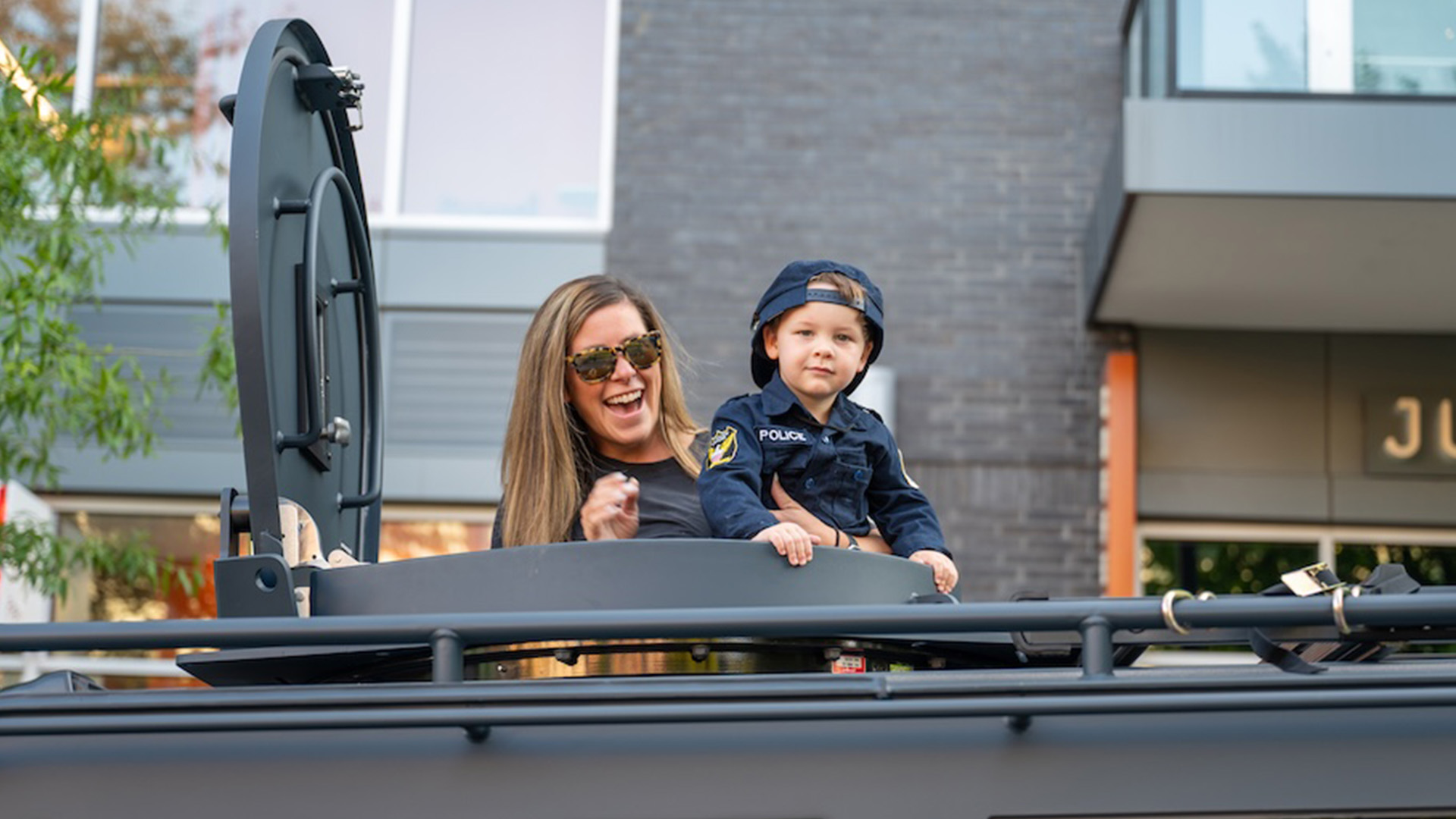 Mother and child poking out of the top of an armoured police vehicle smiling at the camera with thumbs up