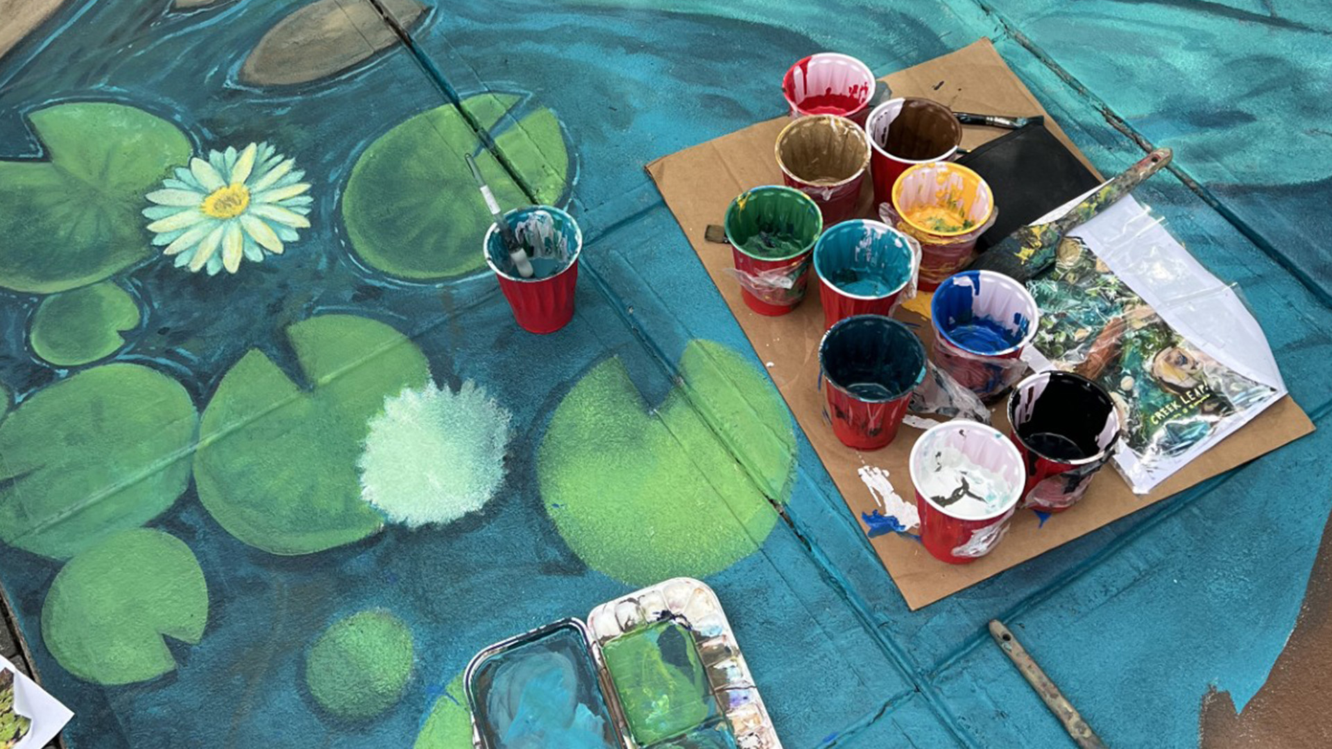 A closeup of the color mural with blues and greens. A tray of different paints sits on top of the mural.