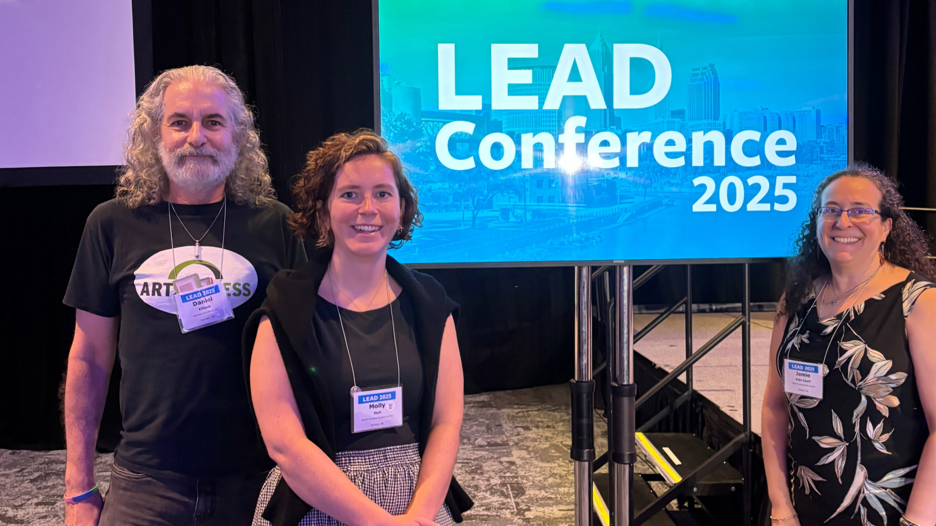 Three presenters standing in front of screen at LEAD conference