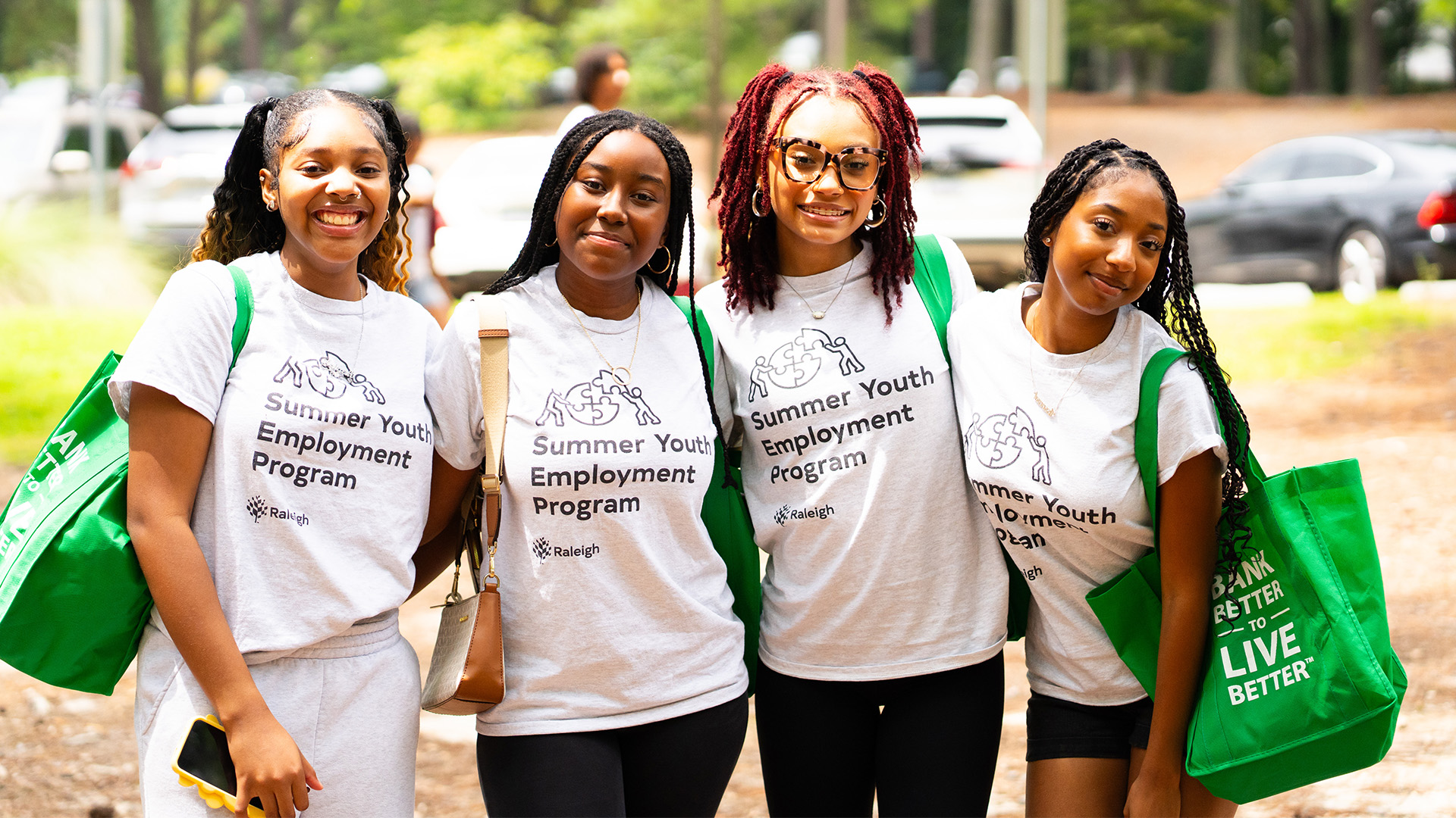 Four participants with arms around each other's shoulders smile at the camera. Each participant is wearing a "Raleigh Youth Employment Program" t-shirt.