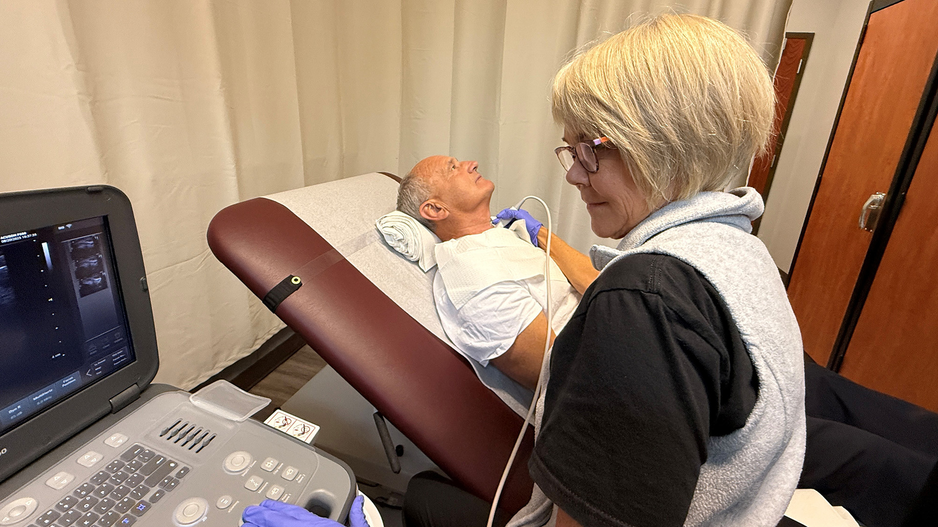 A nurse is using an ultrasound device on a man's neck.