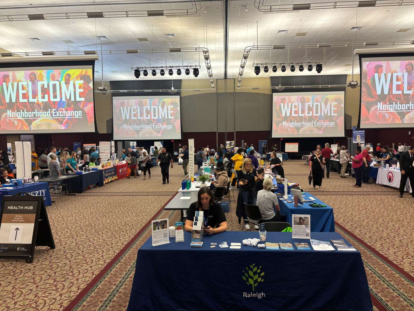 Woman sits behind City of Raleigh table inside an exhibit hall