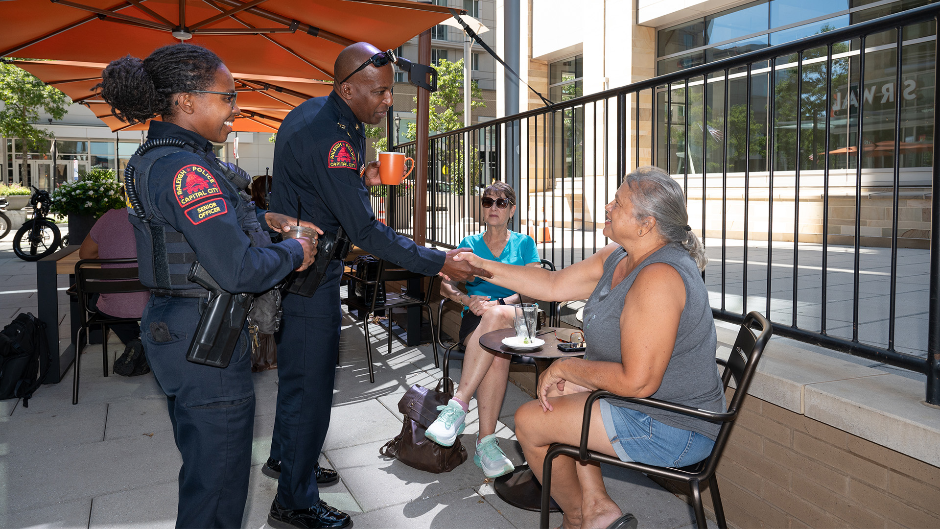 Police Chief Boyce with another RPD officer greets a person sitting at a table having coffee