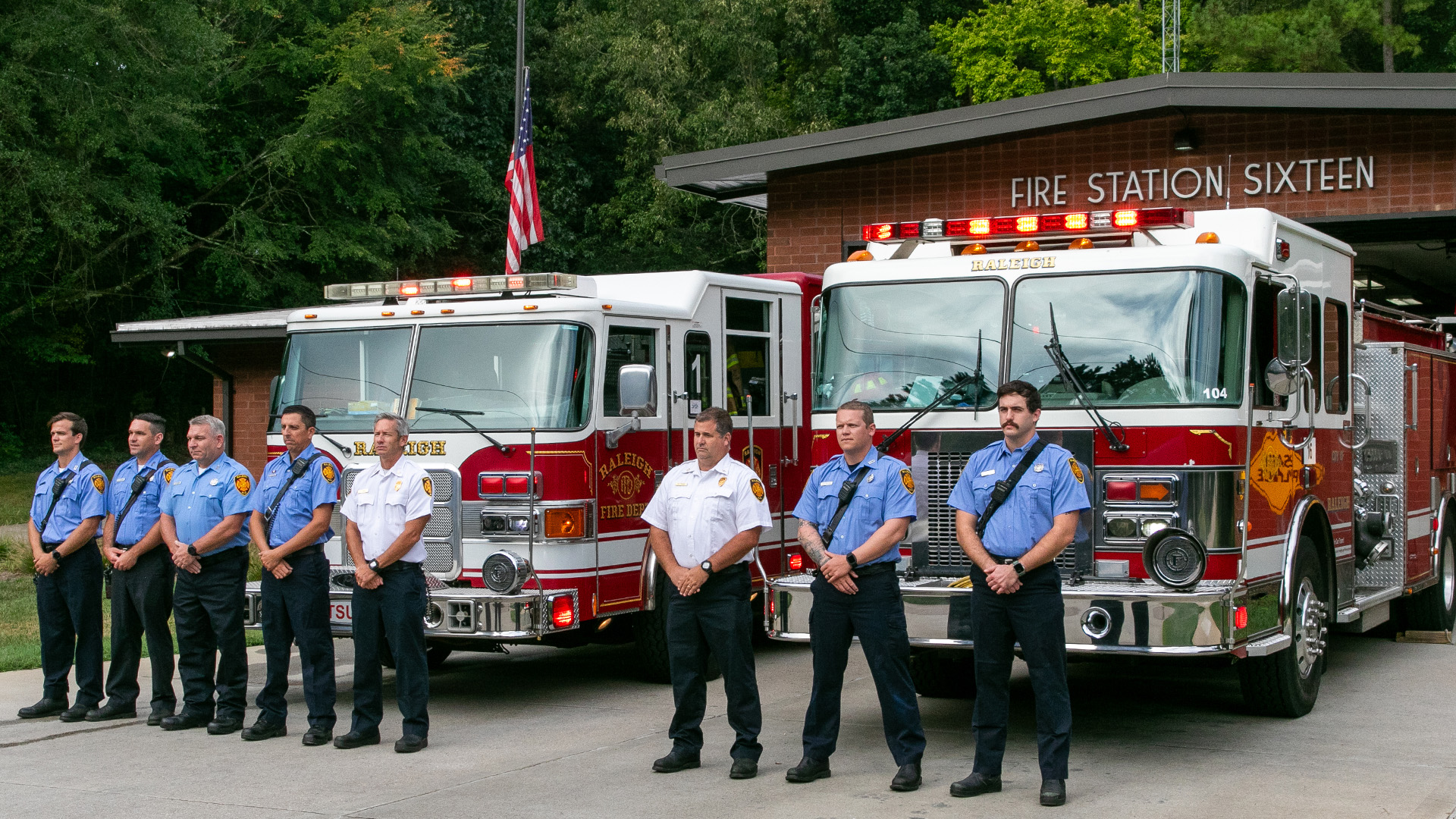 Eight firefighters in uniform stand in front of two fire engines at fire Station Sixteen
