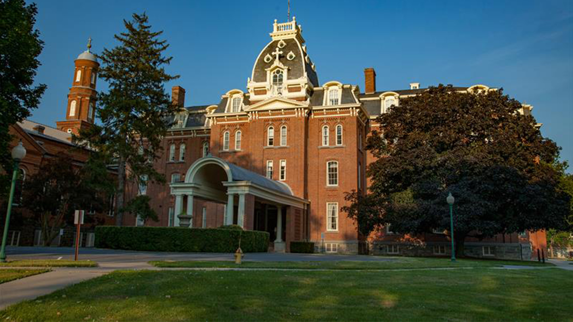 An old brick building with a grande entrance and a green lawn with trees.