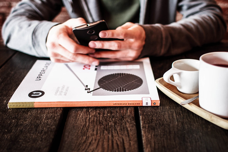 Hands holding a cell phone while sitting at a table with coffee
