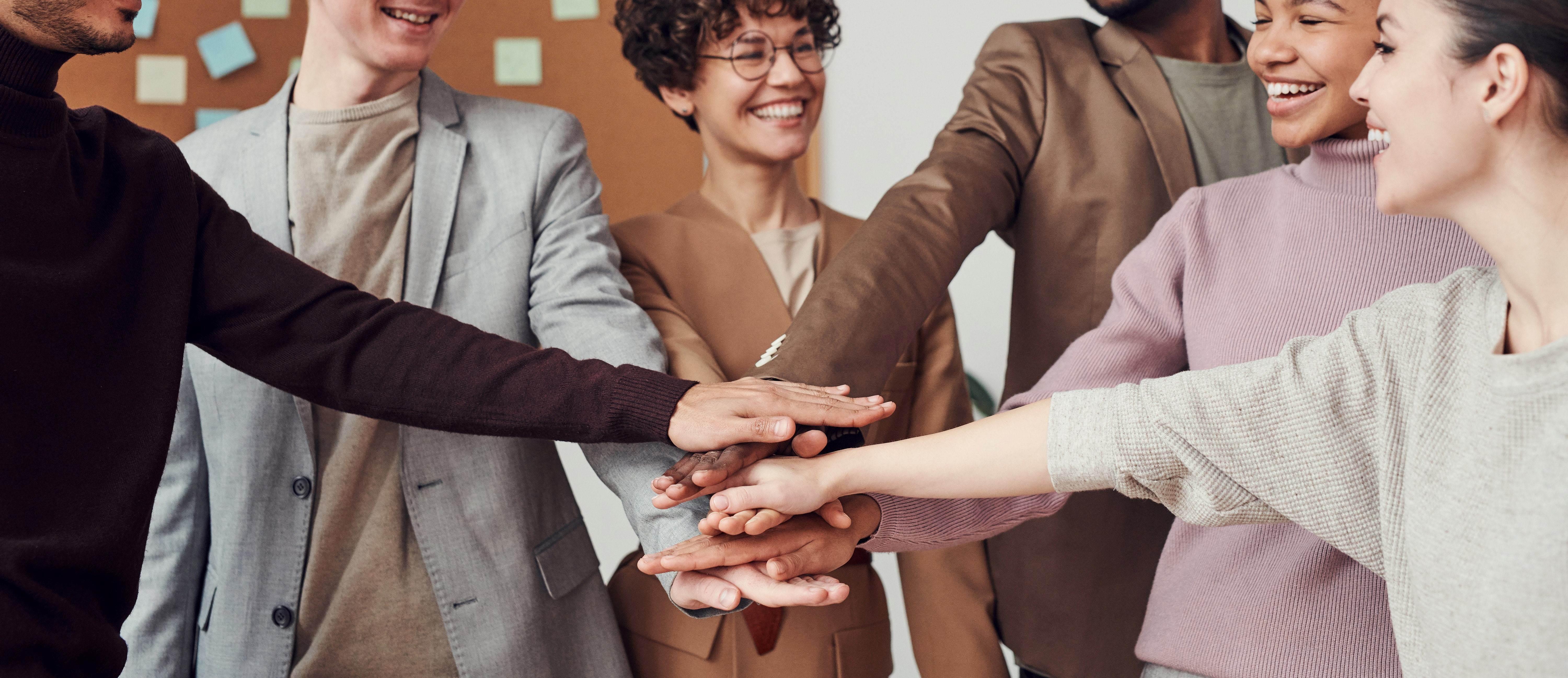 Six people of various backgrounds putting their hands in a huddle