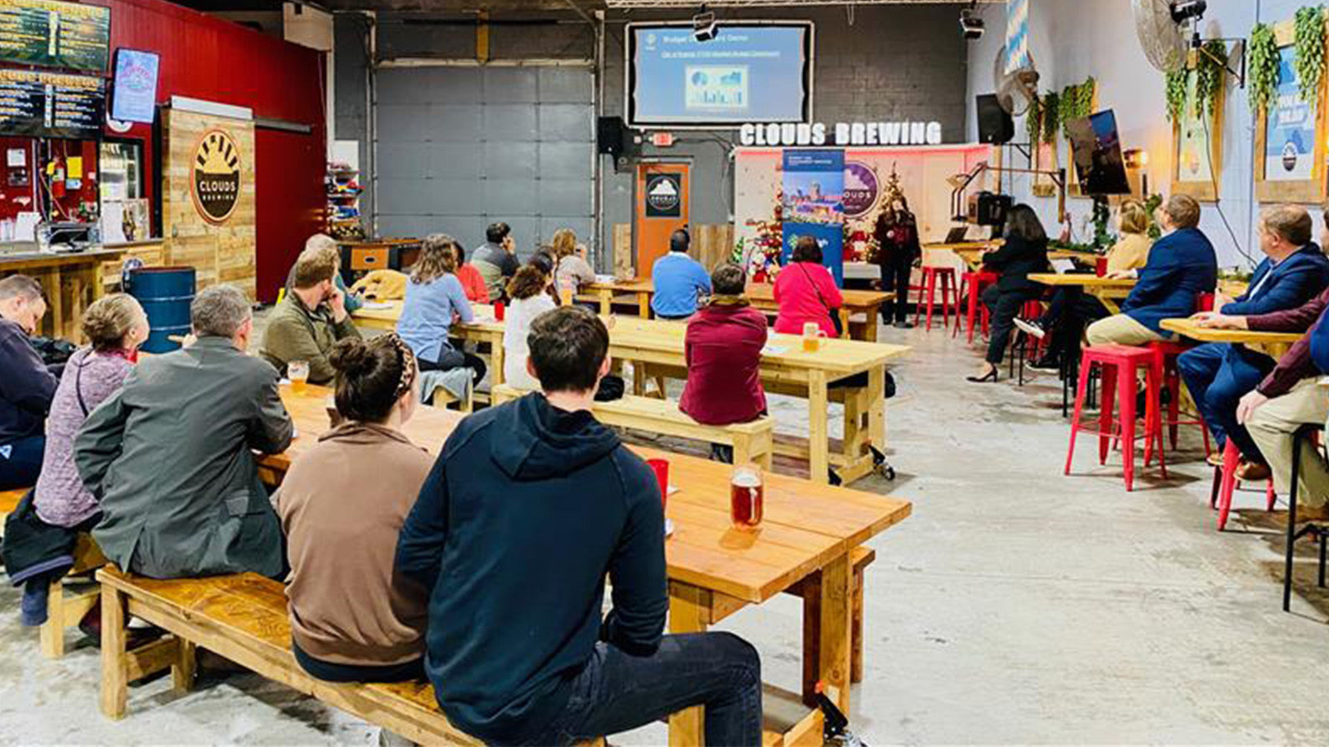 People sitting at tables in a restaurant type place viewing a speaker and a presentation on a screen