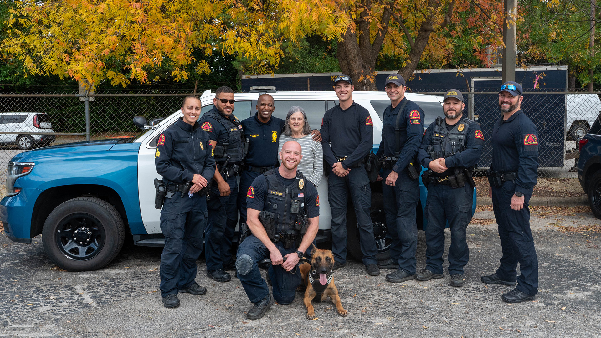Ms. Parker stands with several officers including a officer and K9. A police cruiser is behind the group