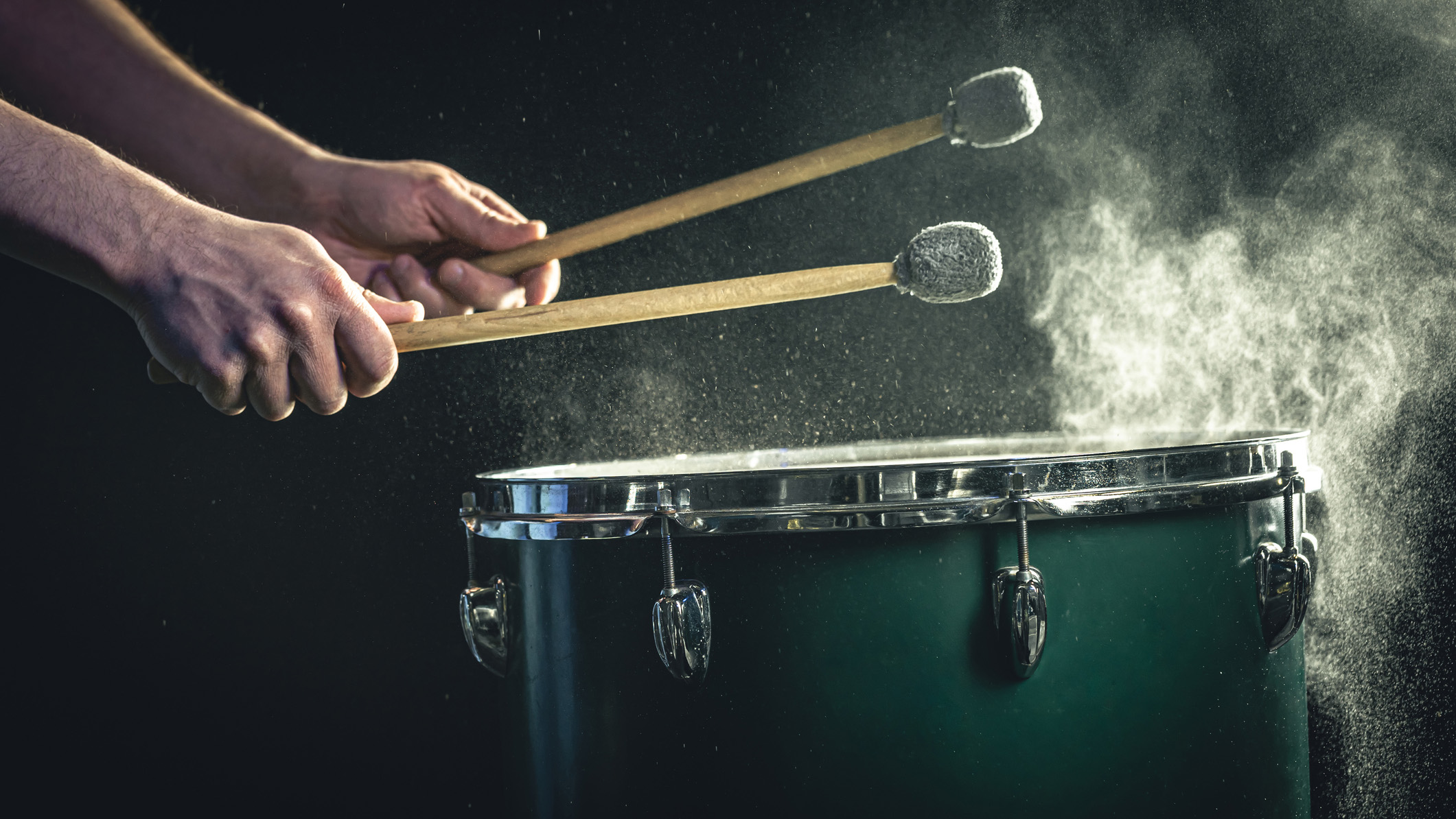 The percussionist plays with sticks on the floor tom on under studio lighting