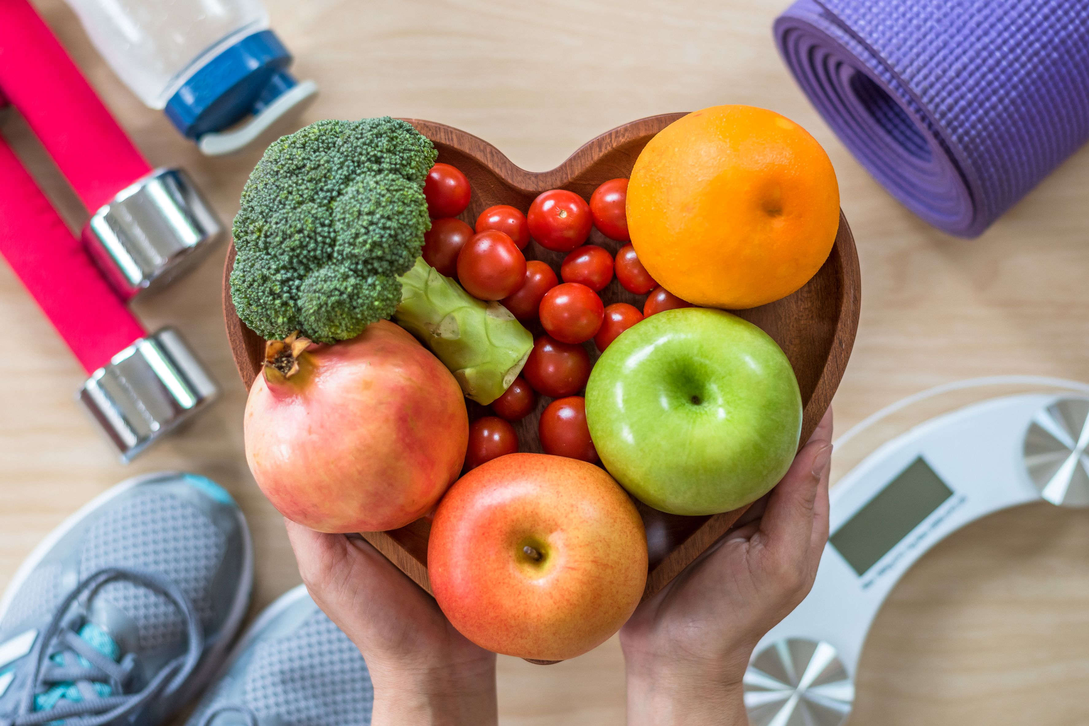 Heart-shaped bowl of fruit and vegetables surrounded by other exercise equipment