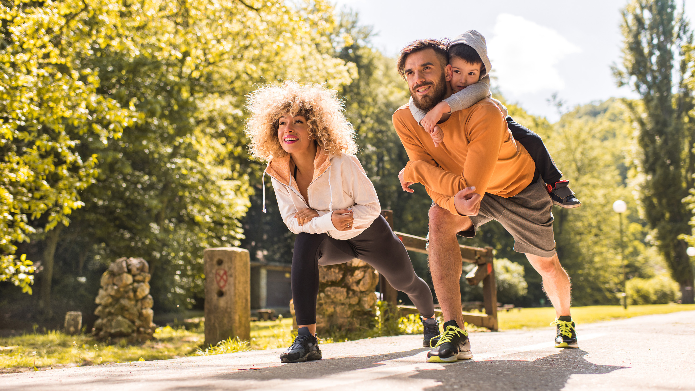 Happy parents stretching in the park while their son is on father's back