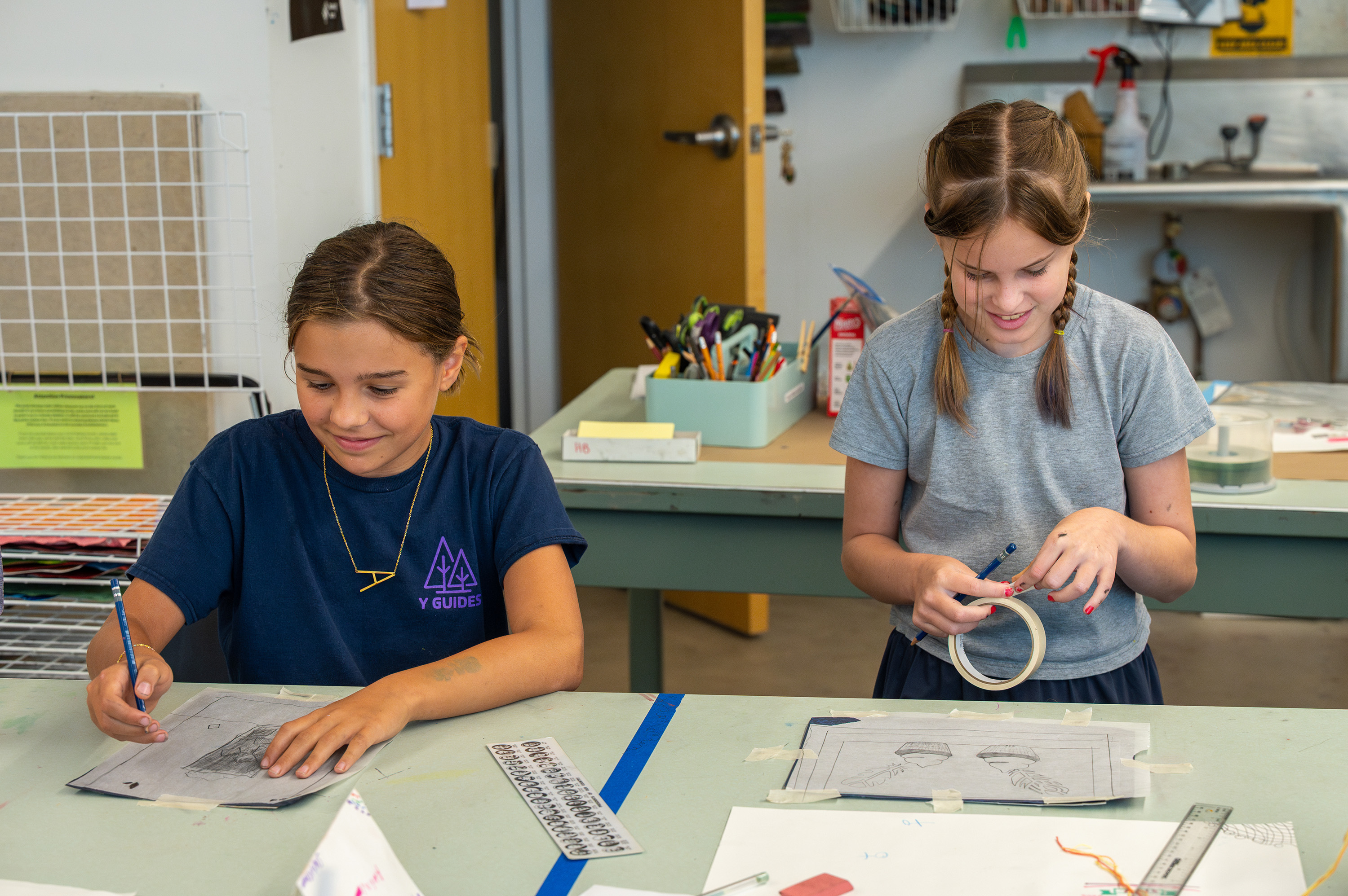 A photograph of two smiling campers working on printmaking projects at a table in the printmaking studio.