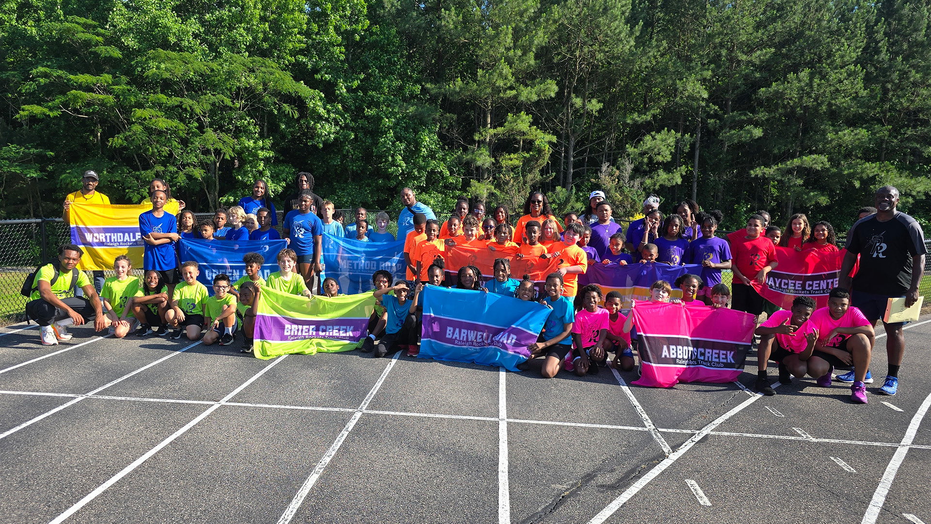 youth track teams with their coaches and signs of their team location
