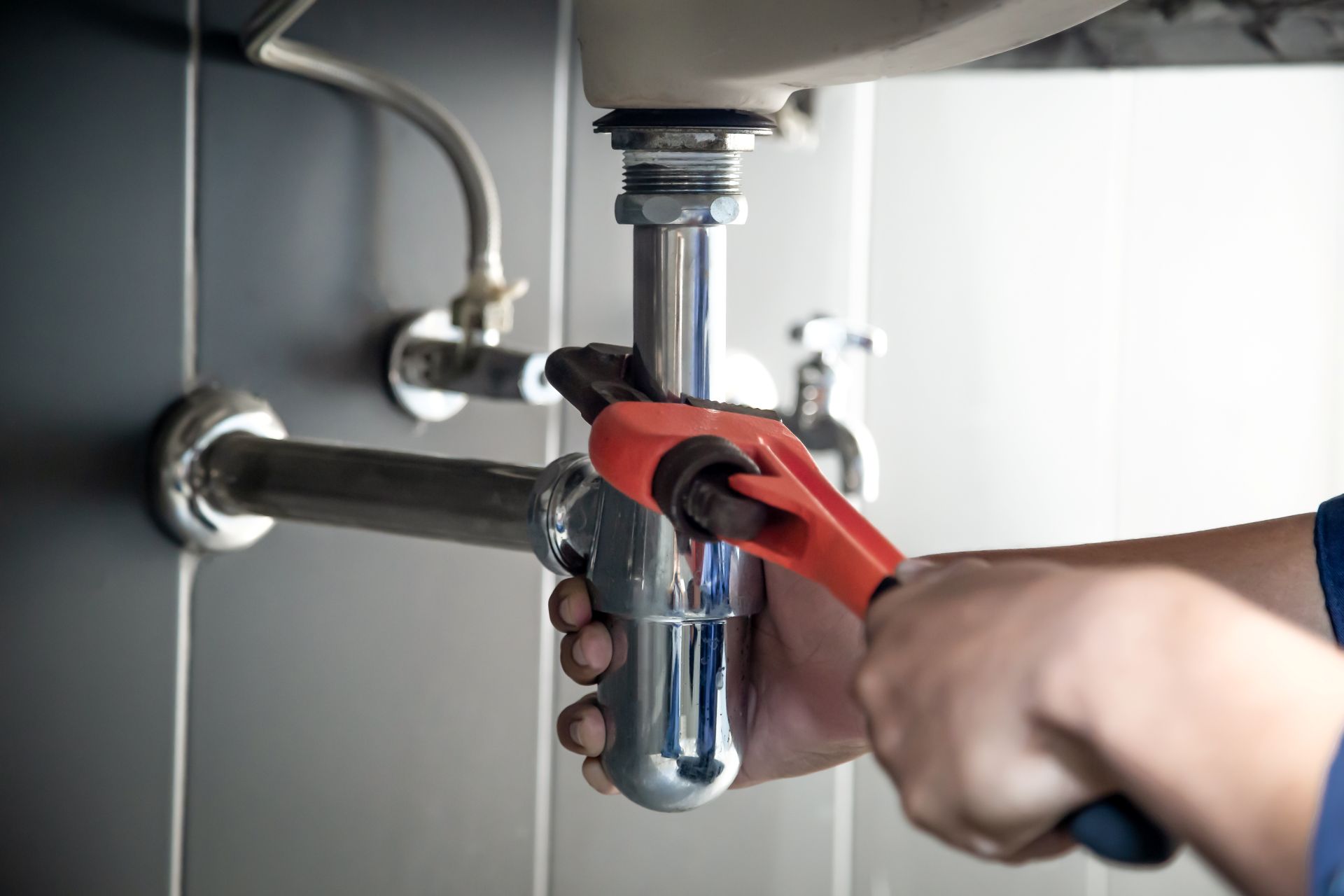 Hand repair under sink leak with red wrench 