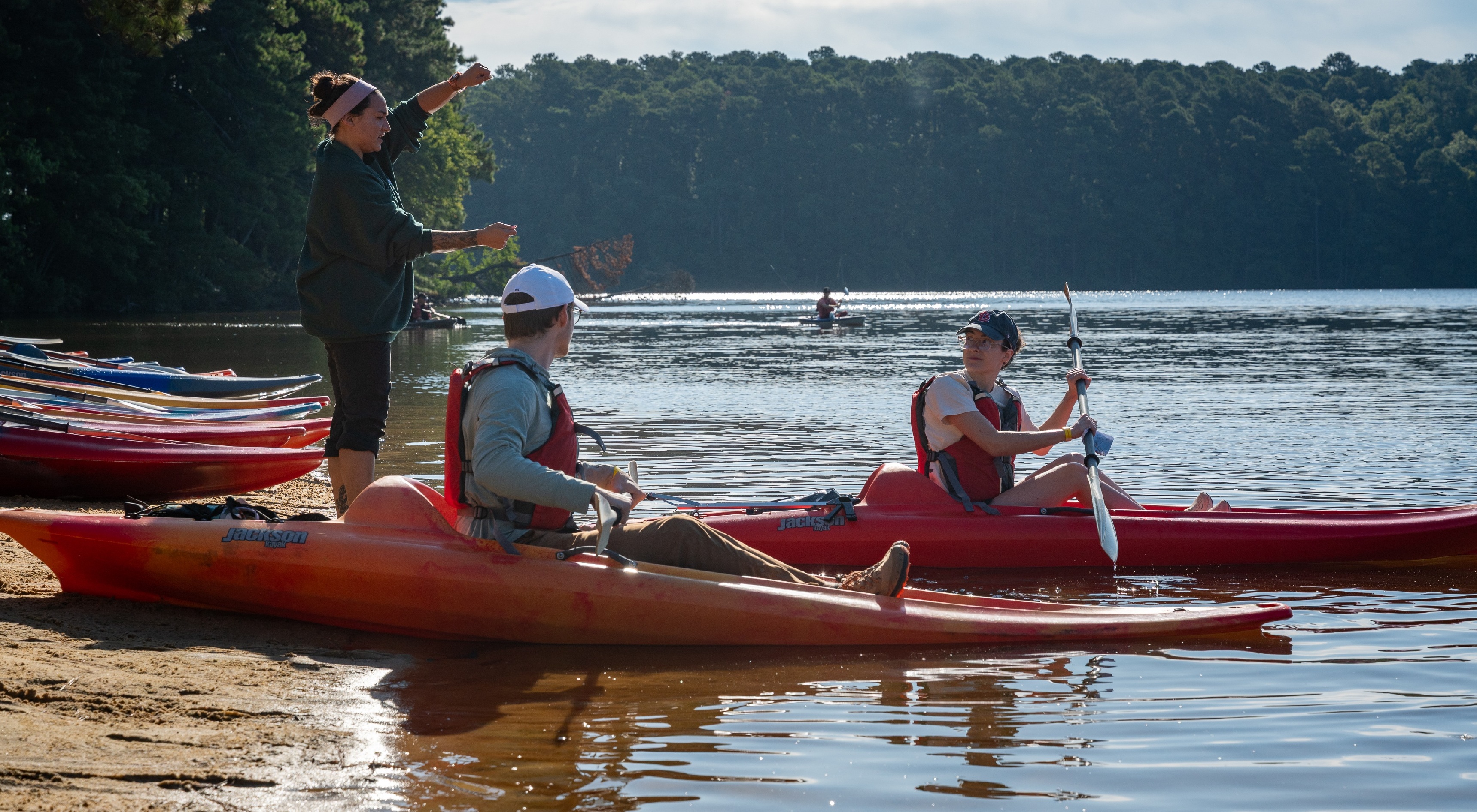two people in a kayak while one is teaching on the shoreline