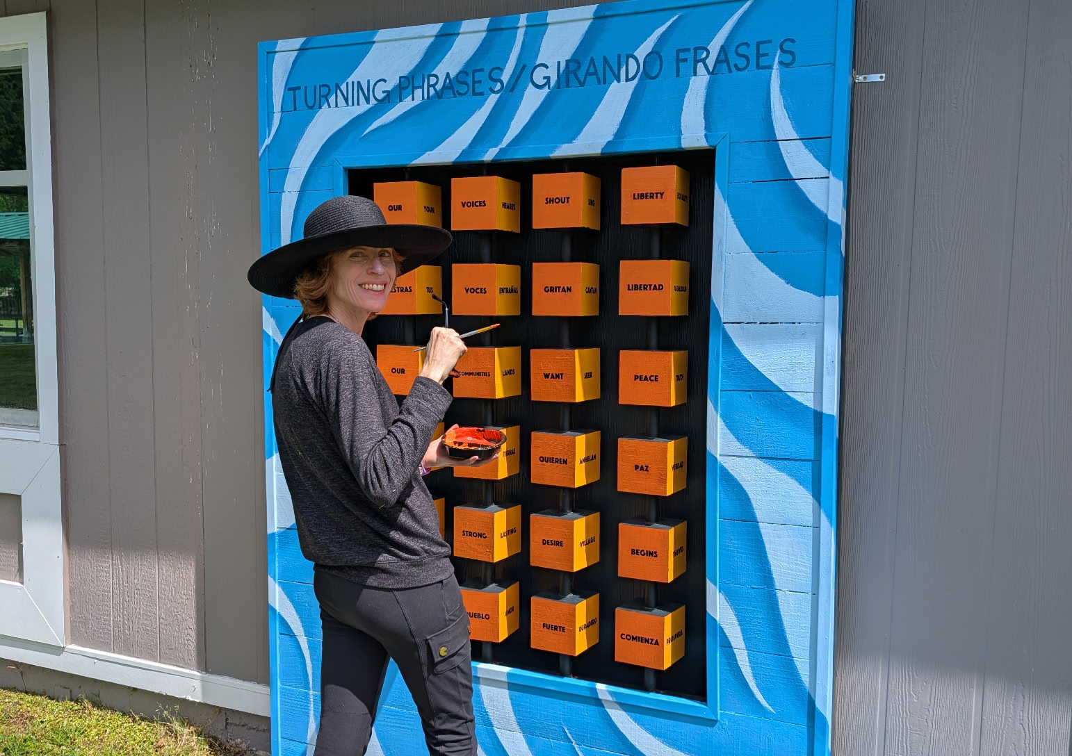 A woman wearing dark clothing stands in front of an interactive poetry sculpture